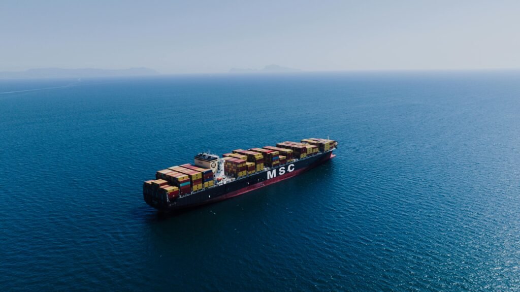 An aerial shot of a loaded container ship sailing near Naples, Italy under clear blue skies.