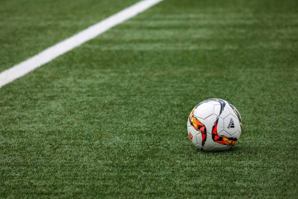 A vibrant soccer ball resting on a pristine grass field beside a white sideline.